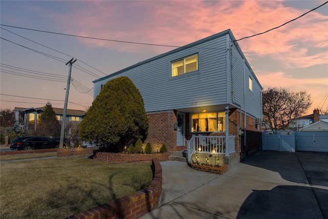 view of front of home with a yard, a gate, fence, and brick siding