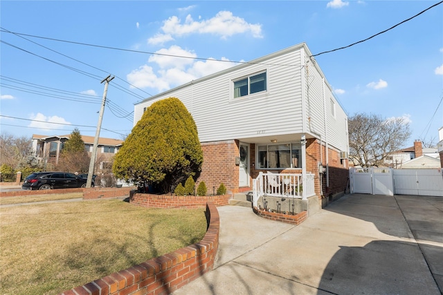 view of front of home with brick siding, concrete driveway, a front yard, a gate, and fence