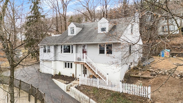 new england style home featuring aphalt driveway, fence, stairway, roof with shingles, and an attached garage