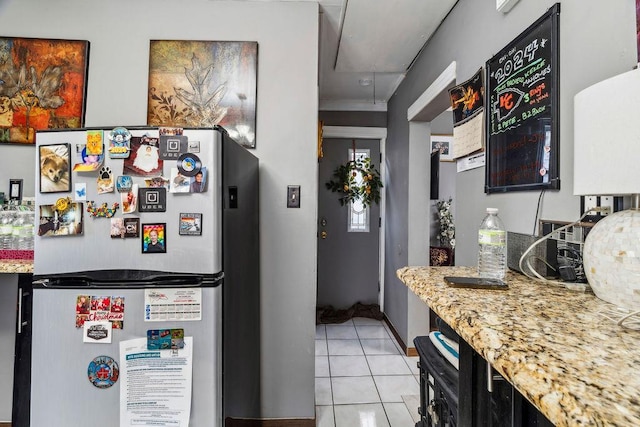 kitchen with light tile patterned floors, freestanding refrigerator, and light stone countertops