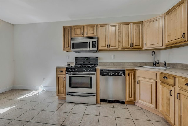 kitchen with light tile patterned floors, light countertops, appliances with stainless steel finishes, a sink, and baseboards