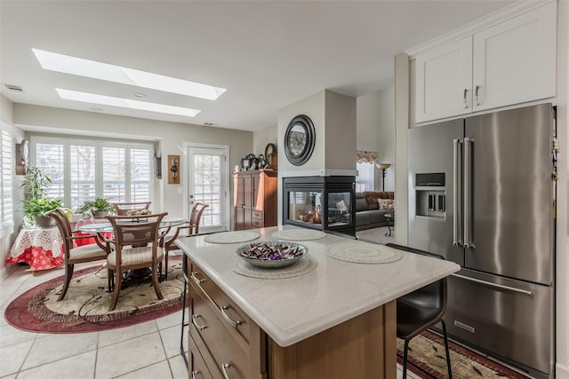 kitchen with high quality fridge, a center island, light tile patterned flooring, white cabinetry, and a multi sided fireplace