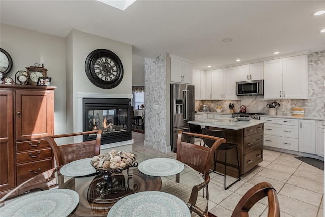 kitchen featuring light tile patterned floors, stainless steel appliances, a multi sided fireplace, light countertops, and backsplash