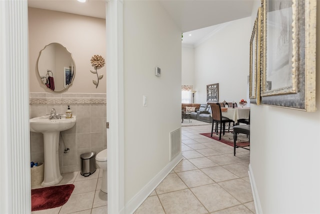 corridor featuring crown molding, tile walls, visible vents, light tile patterned flooring, and a sink