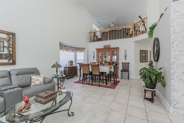 living area with light tile patterned floors, baseboards, a towering ceiling, ceiling fan, and ornamental molding