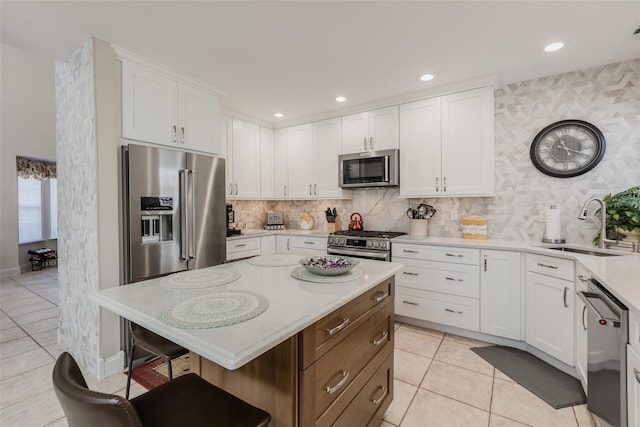 kitchen with a breakfast bar, light tile patterned floors, appliances with stainless steel finishes, white cabinetry, and a sink