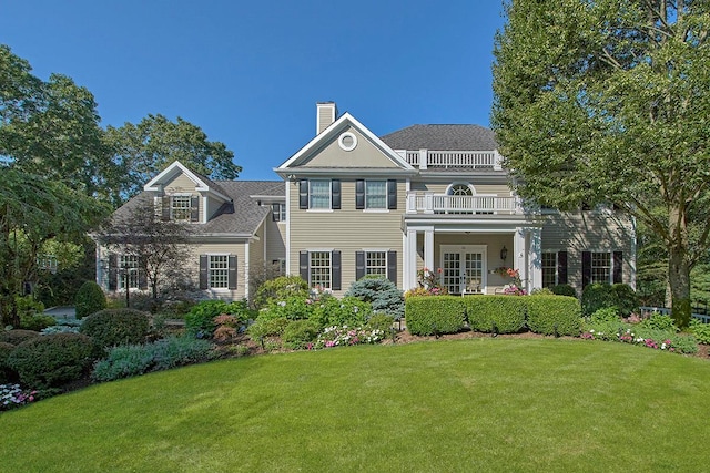 view of front of property with french doors, a chimney, a front yard, and a balcony