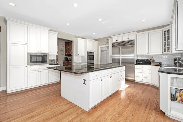 kitchen featuring built in appliances, light wood-style flooring, a kitchen island, white cabinets, and glass insert cabinets