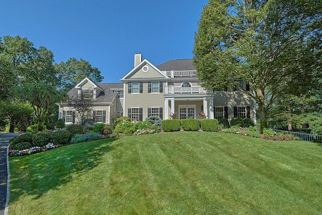 georgian-style home with a balcony, a chimney, and a front lawn