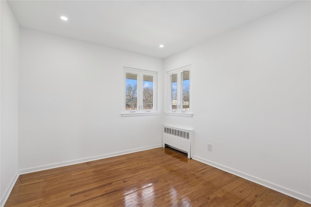 unfurnished room with recessed lighting, radiator heating unit, wood-type flooring, and baseboards