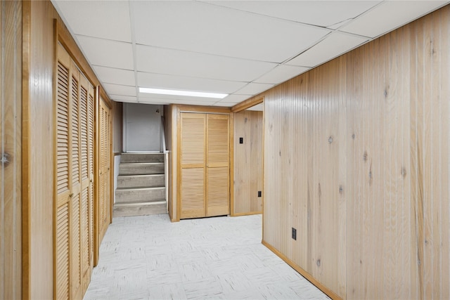 corridor featuring a drop ceiling, wood walls, and stairs