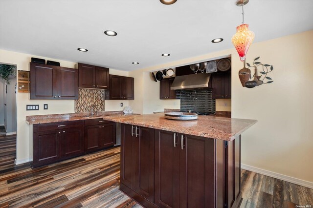 kitchen featuring dark wood-style floors, wall chimney range hood, a sink, and tasteful backsplash