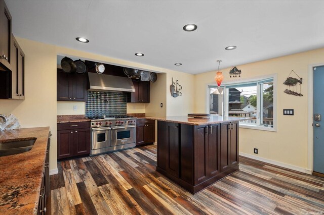 kitchen featuring a sink, range with two ovens, wall chimney range hood, and dark wood-style floors