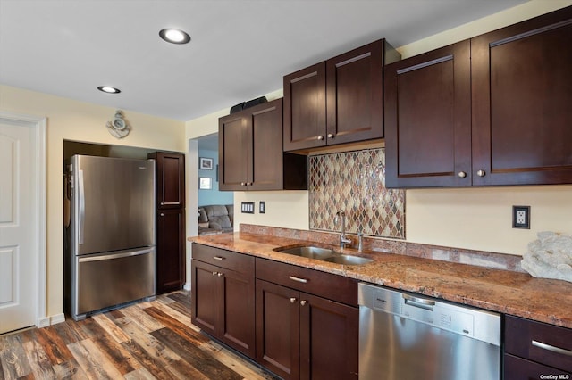 kitchen with light stone counters, dark brown cabinetry, stainless steel appliances, a sink, and dark wood-style floors