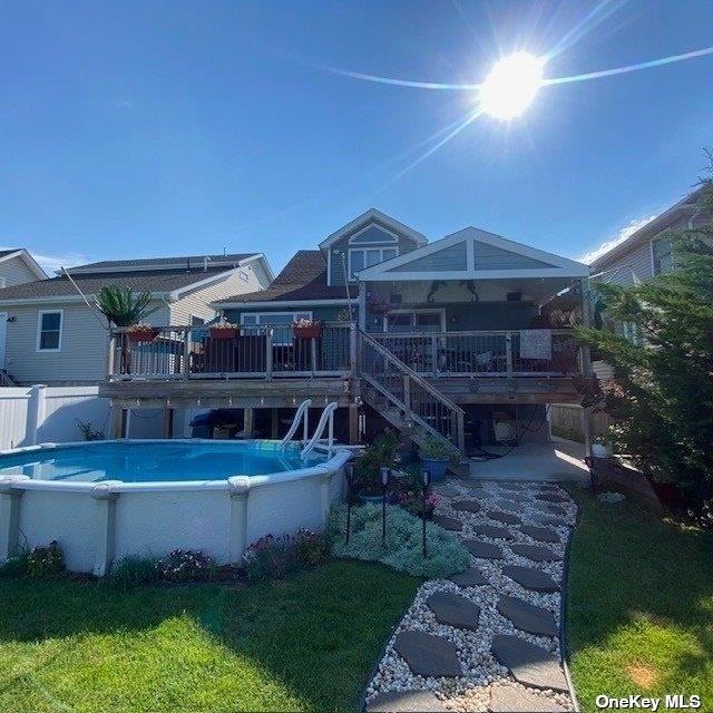 rear view of house featuring stairway, a wooden deck, and a fenced in pool