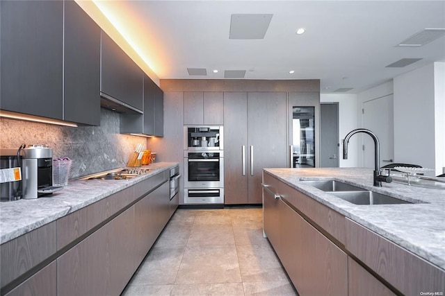 kitchen featuring light stone counters, tasteful backsplash, recessed lighting, appliances with stainless steel finishes, and a sink