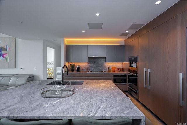 kitchen with tasteful backsplash, cooktop, a sink, modern cabinets, and oven