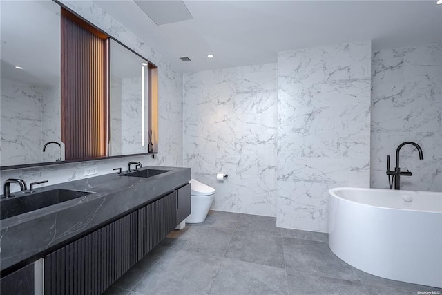 full bath with double vanity, stone wall, a freestanding tub, and a sink