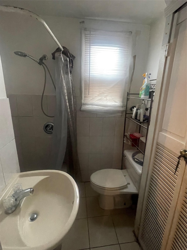 full bath with a shower with shower curtain, toilet, tile patterned floors, a sink, and tile walls