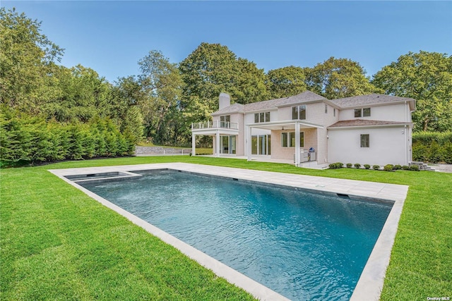 rear view of house featuring a chimney, a balcony, a patio, an outdoor pool, and a yard