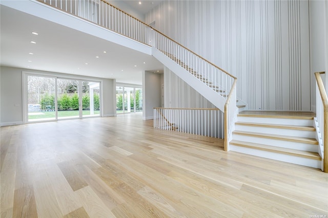 unfurnished living room with baseboards, stairs, wood finished floors, recessed lighting, and a high ceiling