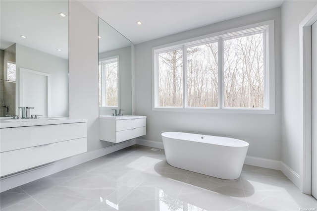 full bath featuring a soaking tub, two vanities, baseboards, and recessed lighting