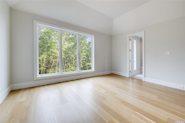 spare room featuring baseboards, vaulted ceiling, and light wood-style floors