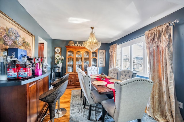 dining room with light wood-style flooring, a bar, and an inviting chandelier