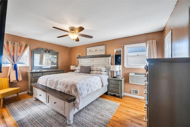 bedroom with light wood-type flooring, baseboards, visible vents, and a wall mounted AC