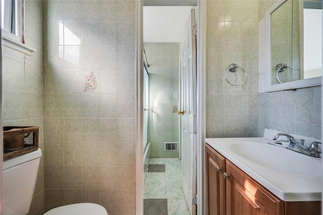 bathroom with toilet, vanity, visible vents, tile walls, and a shower with door