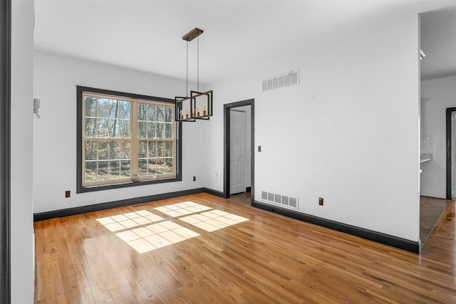 unfurnished dining area featuring visible vents, baseboards, an inviting chandelier, and hardwood / wood-style floors