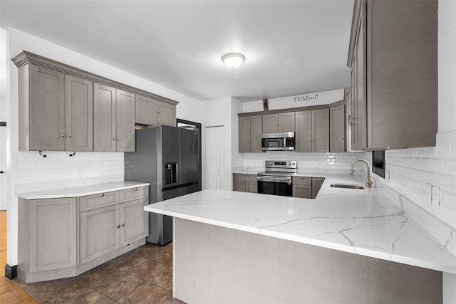 kitchen with a sink, appliances with stainless steel finishes, a peninsula, decorative backsplash, and light stone countertops