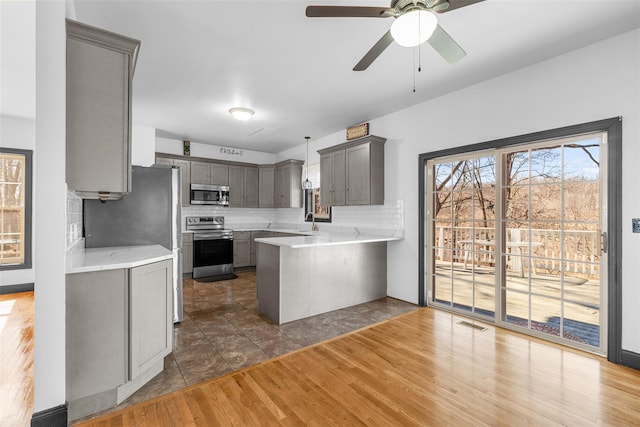 kitchen featuring gray cabinets, dark wood finished floors, appliances with stainless steel finishes, a peninsula, and light countertops