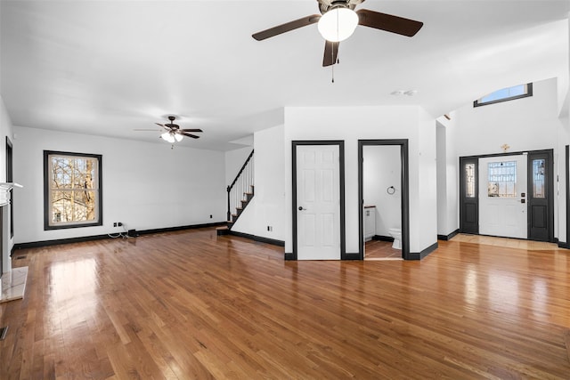 unfurnished living room with a fireplace with raised hearth, a healthy amount of sunlight, stairs, and hardwood / wood-style flooring