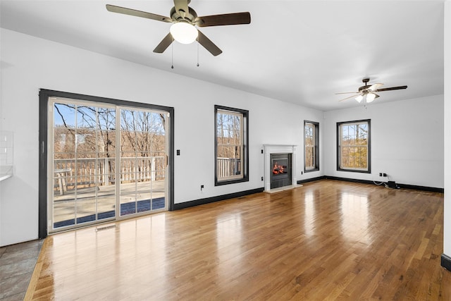 unfurnished living room featuring a glass covered fireplace, visible vents, wood finished floors, and baseboards