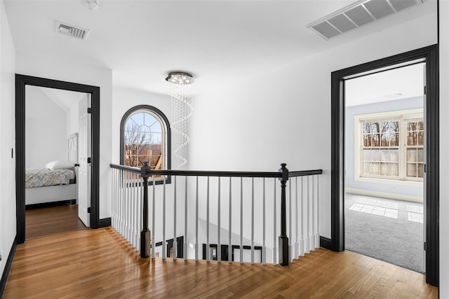 hall with an upstairs landing, visible vents, and wood finished floors