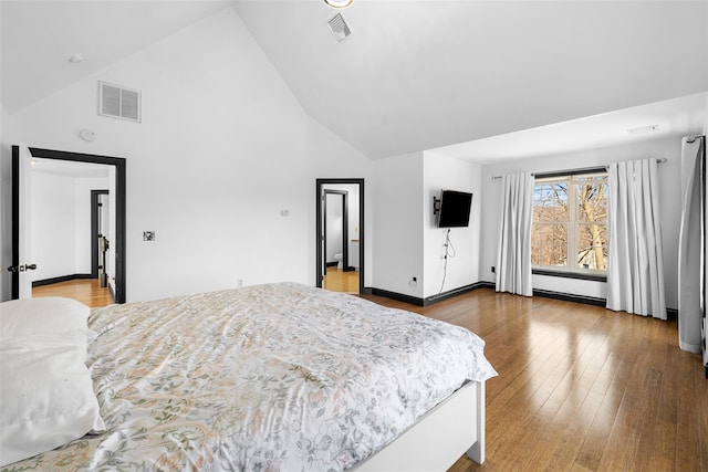 bedroom with visible vents, wood-type flooring, high vaulted ceiling, and baseboard heating