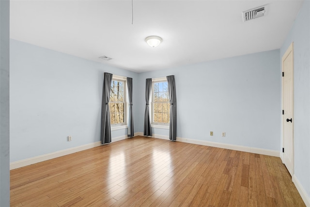 spare room with light wood-type flooring, visible vents, and baseboards