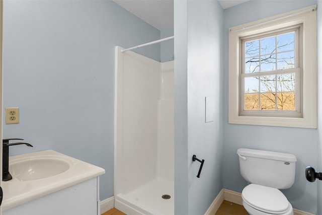 bathroom featuring a stall shower, toilet, baseboards, and a sink