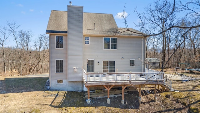 back of property featuring a shingled roof, a wooden deck, a trampoline, and a chimney