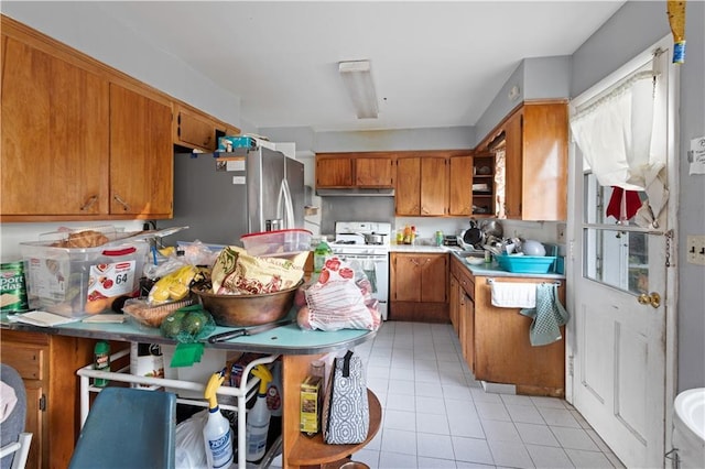 kitchen featuring light tile patterned floors, light countertops, freestanding refrigerator, brown cabinetry, and white gas range