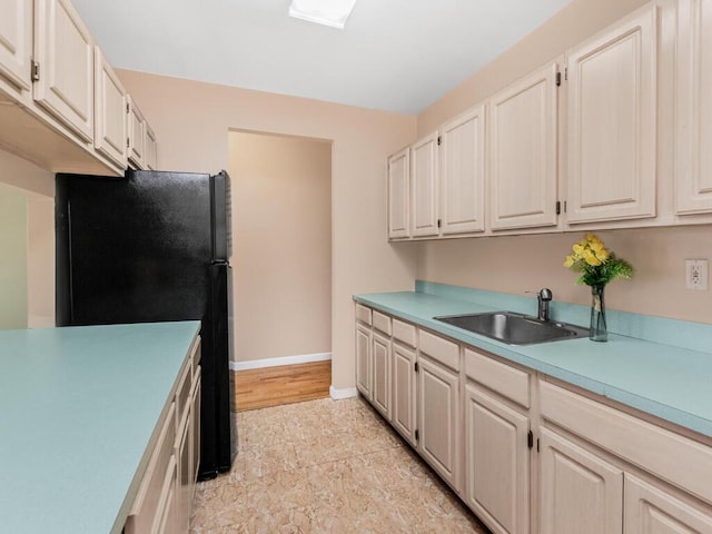 kitchen featuring freestanding refrigerator, light countertops, a sink, and baseboards