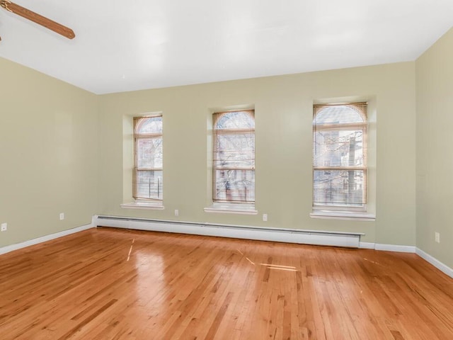 spare room with baseboard heating, a wealth of natural light, and wood finished floors