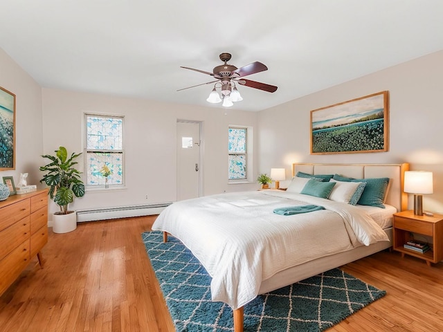 bedroom with a ceiling fan, a baseboard heating unit, and wood finished floors