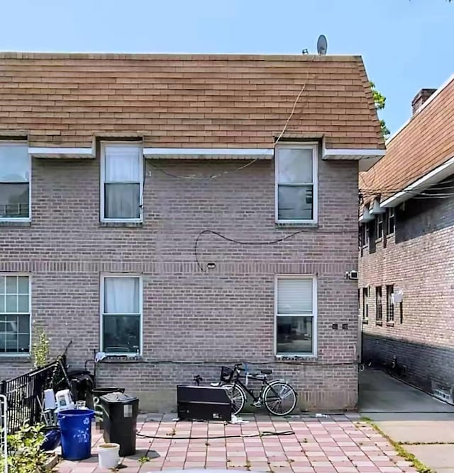 rear view of property featuring a patio, brick siding, and roof with shingles