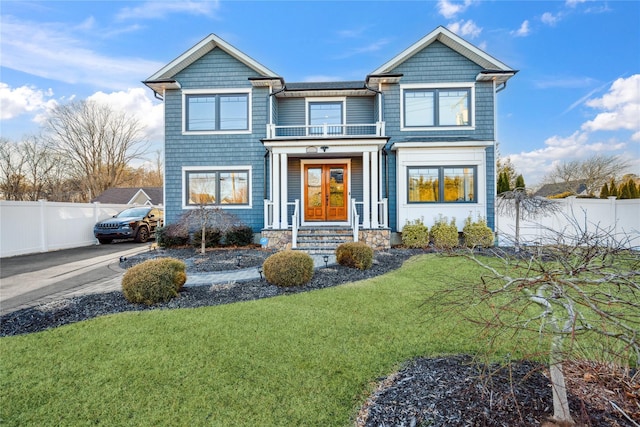 view of front of house featuring a balcony, fence, a front lawn, french doors, and aphalt driveway