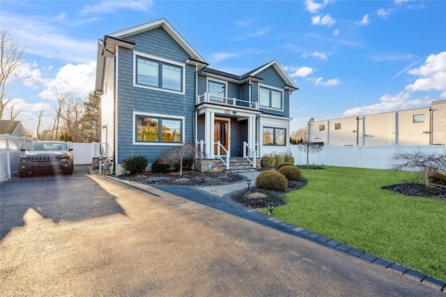 view of front facade featuring a front lawn, a balcony, driveway, and fence