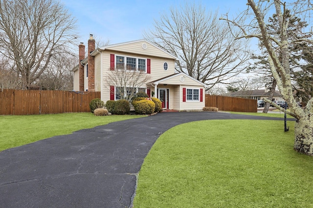 traditional home featuring driveway, a chimney, a front yard, and fence