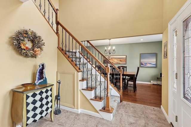 stairs featuring a chandelier, a baseboard heating unit, wood finished floors, a towering ceiling, and baseboards