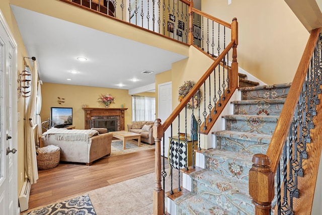 stairway featuring visible vents, a towering ceiling, wood finished floors, a brick fireplace, and recessed lighting